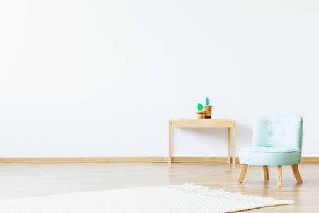 Small wooden table with decorative cactuses, white carpet and mint chair for baby in bright kid room interior. Place your product hereの写真素材