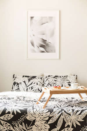 Poster above bed with patterned sheets and wooden tray in white hotel bedroom interior. Real photoの写真素材