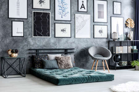 Grey armchair next to green futon in modern living room interior with postersの写真素材