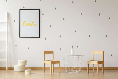 White table between wooden chairs in child's room interior with poster on bright wallpaper. Real photoの写真素材