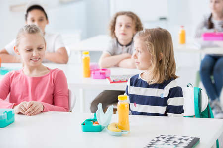 Smiling girl and friend eating lunch during break at school