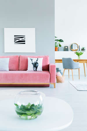Apartment interior for a freelancer with a gray armchair and wooden desk in the background and a painting above pink sofa in the living room. Real photoの写真素材