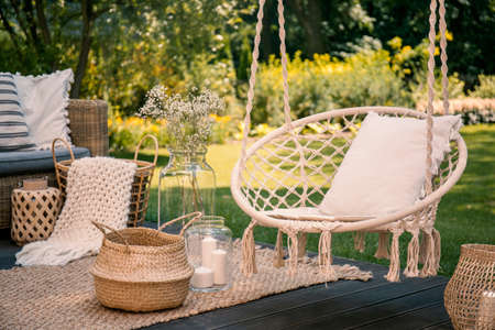 Pillow on hanging chair and basket on carpet in the garden with flowers. Real photoの写真素材