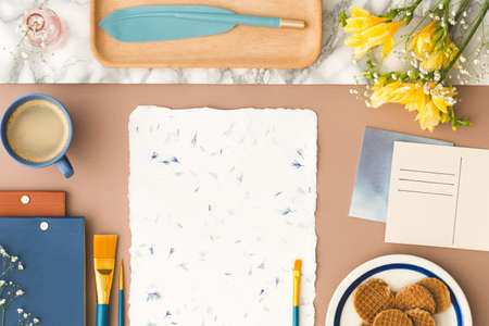 Top view on desk with yellow flowers, paint brush on paper and cup of coffee. Real photo with an...