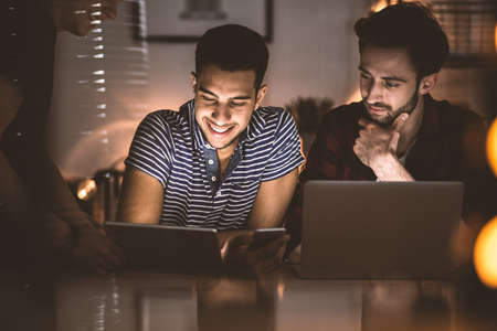 Smiling friends uploading photos on social networking site while using smartphoneの写真素材