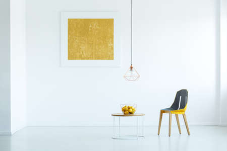 Real photo of a chair standing next to a table with fruit in white simple living room interior with...