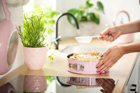 Close-up of woman's hands sprinkling powdered sugar on a cake on a kitchen countertop