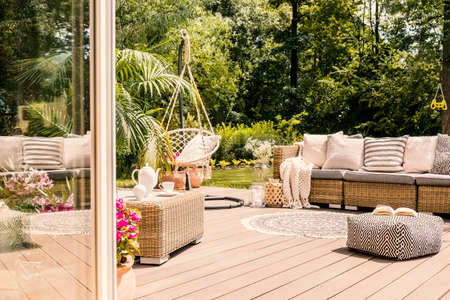 Pouf and rattan sofa on wooden patio with hanging chair in the garden. Real photoの写真素材