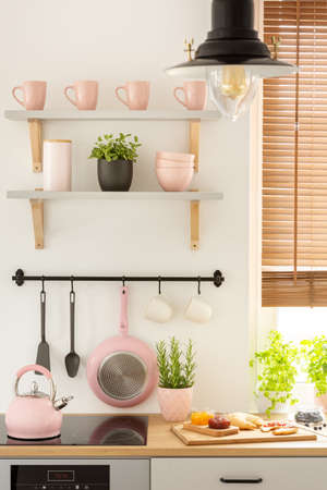Close-up of pink kitchen tools, shelves with mugs and wooden board with food in a kitchen interior. Real photoの写真素材