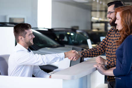 Car dealer and buyer shaking hands after transaction in luxury dealing salonの写真素材