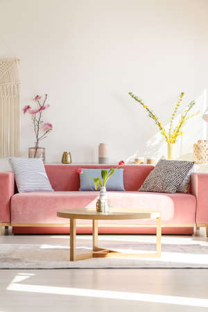 Cushions on red settee and wooden table in living room interior with flowers. Real photoの写真素材