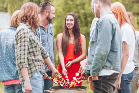 Happy woman grilling shashlik with friends during birthday party in the gardenの写真素材