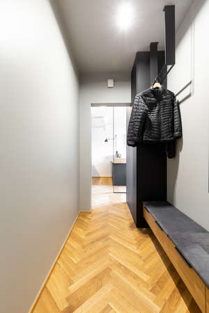Black coats on a creative, industrial hanger in an entrance interior with wooden bench, gray walls and herringbone parquet floorの写真素材