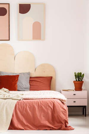 Plant on cabinet next to bed with pillows in bedroom interior with posters on white wall. Real photoの写真素材