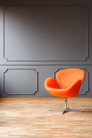 Modern orange armchair in minimal grey living room interior with wooden floor. Real photo with a place for your furnitureの写真素材