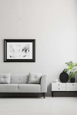 Photo in a black, thick frame on a gray wall, white sideboard and a comfy sofa in a stylish living...