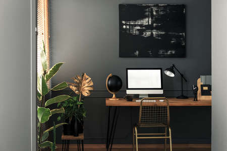 Painting above desk with desktop computer and lamp in grey and gold workspace interior. Real photo