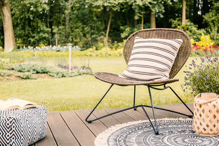 Real photo of a modern garden chair with a white, striped pillow standing on a wooden deck in the...