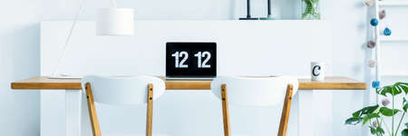 Trendy home office area with a laptop on a wooden desk in a bright living room interior with a...