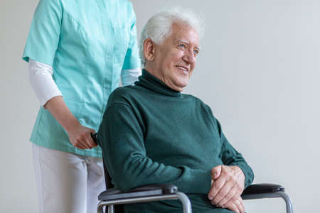 Happy senior man in the wheelchair and nurse helping him
