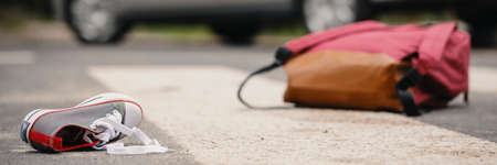 Car accident concept - an empty crosswalk with a child's shoe and backpack lying on the road and a vehicle in the backgroundの写真素材