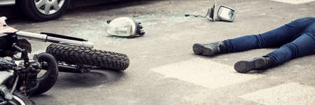 Fatal aftermath of a car accident concept - dead body and crashed motorcycle parts lying on the roadのeditorial素材