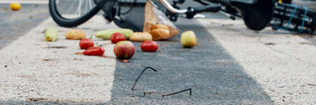 Glasses, groceries and a bicycle on an empty road crossing - panorama of a dangerous car accident conceptの写真素材