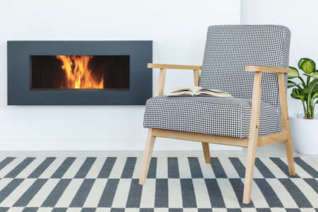 Retro armchair with a book next to a fireplace set on a striped carpetの写真素材