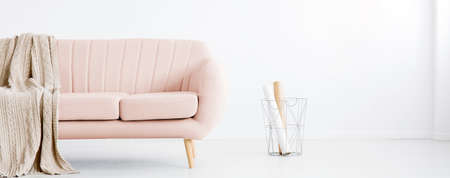 Real photo of white living room interior with metal basket with paper rolls and pastel pink couch with coverlet. Place for your armchairの写真素材