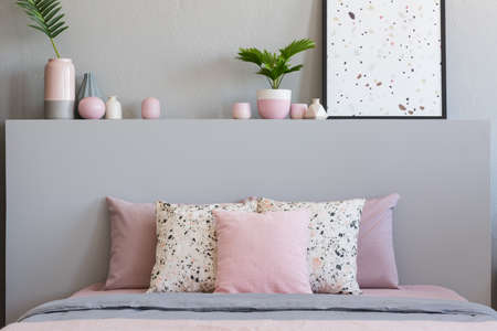 Pink and patterned pillows on bed with headboard in grey bedroom interior with poster. Real photoの写真素材