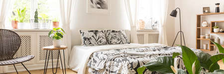 A cozy double bed by a white wall between two windows in a bright, natural bedroom interior with...