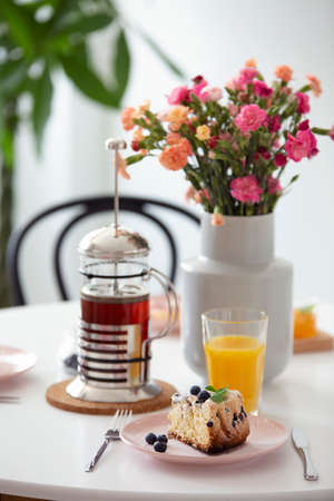 Flowers and orange juice on table with tea and dessert in a restaurant interior. Real photo