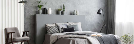 Black metal lamp standing next to double bed with grey sheets in monochromatic bedroom interior with...