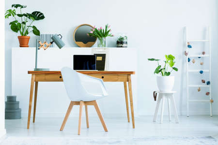 Real photo of wooden home office desk with metal lamp and empty laptop standing in white living room...