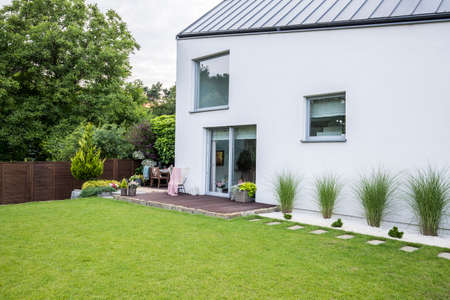 Plants, flowers and garden furniture on a wooden terrace outside of a contemporary suburban house...