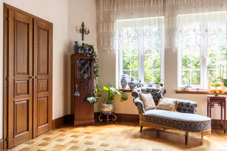 Real photo of a living room interior with a chaise longue, porcelain vases, wooden door and windows with curtainsの写真素材