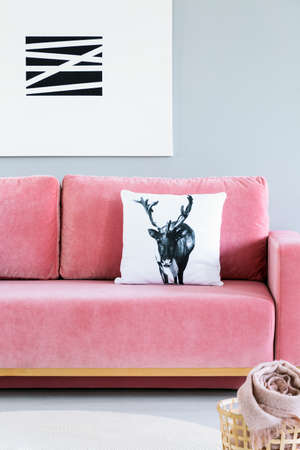 Pillow with deer case placed on pink velvet sofa in the real photo of bright living room interior with modern poster on the wallの写真素材