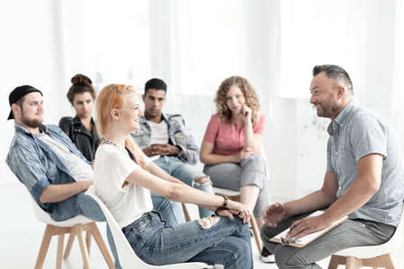 Smiling red-haired girl talking to a therapist during meeting for difficult teenagers