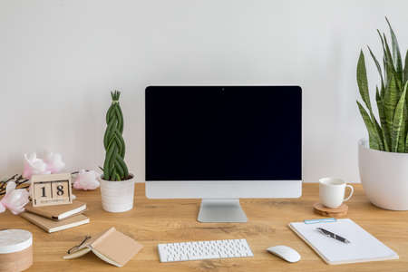 Desktop computer with mockup on wooden desk with books, keyboard and plants in the interior. Real...