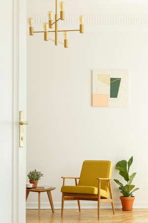 Comfortable yellow chair with a wooden frame in a tall and spacious living room interior with a poster on the white wall. Real photoの写真素材