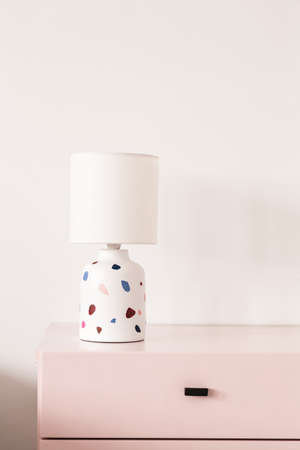 Patterned lamp on pastel pink cabinet against white wall in colorful interior. Real photoの写真素材