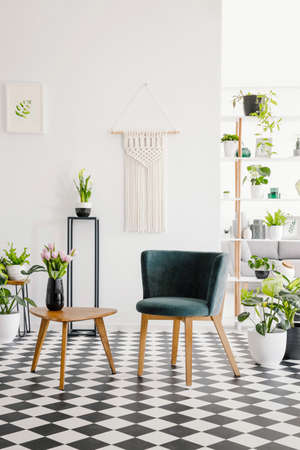 Modern seat and retro coffee table on a checkered floor in a botanical living room interior. Real...