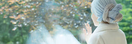 Panorama of sick woman with cancer touching window in the hospice during treatmentの写真素材