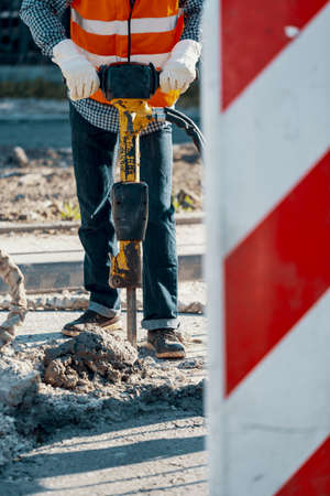 Worker in reflective vest and with drill repairing asphalt during roadworksの写真素材