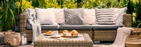 Cushions on settee and rattan table on patio in the garden during summer. Real photoの写真素材
