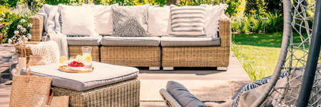 Panorama of rattan sofa with pillows and table on terrace in the garden. Real photo