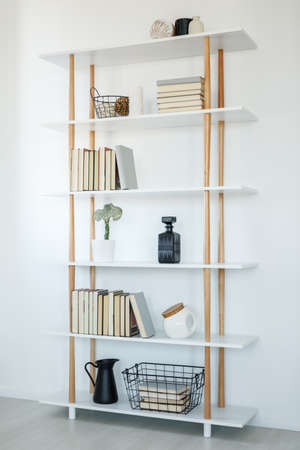 Books on white wooden shelves in simple living room interior. Real photoの写真素材