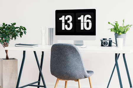 Real photo of a grey chair next to a desk with a computer, camera and plant in a home office interiorの写真素材