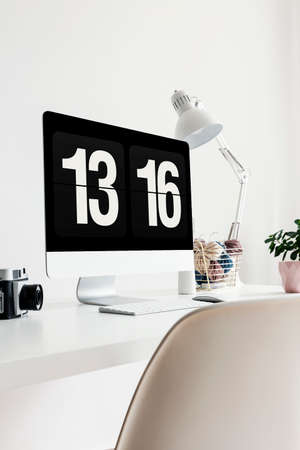 Close-up of a screen showing time on a white desk with a lamp, camera and plant in an office...