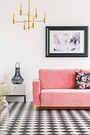 Checkered tiles in a living room interior with a pink sofa, poster and golden lamp. Real photoの写真素材